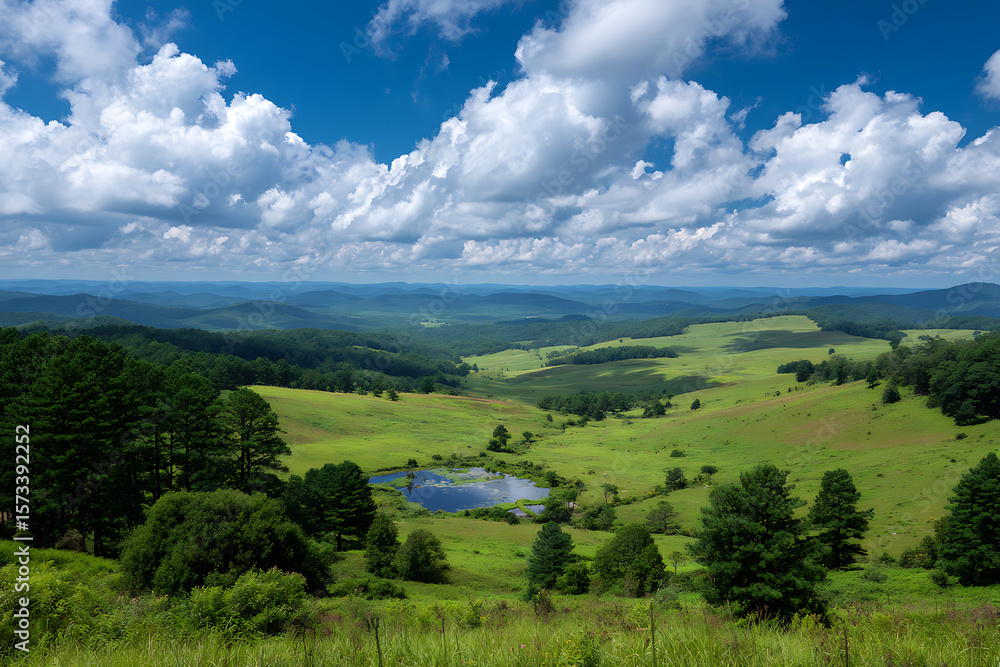 Obraz premium Scenic Vista of Rolling Green Hills and a Small Pond Under a Bright Blue Sky with Puffy White Clouds Lush Greenery and Distant Mountains