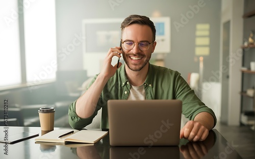 Happy business man working from home talking on phone with laptop and notebook on desk for remote work