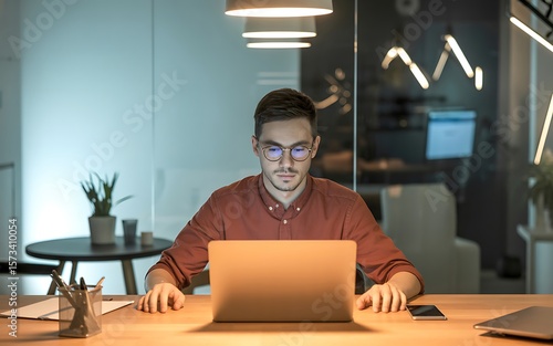 Focused young man working late at his laptop in a modern office, a picture of determination and concentration.