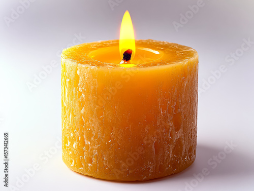 Candle with a yellow wax and a red wick is lit. The candle is sitting on a white surface