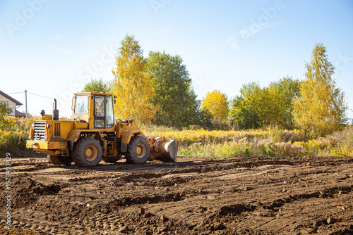Yellow bulldozer at a construction site. Big wheel excavator leveling and clearing the land plot side view. Moving earthworks soil. Copy space. Building area. Special transport. High quality photo.