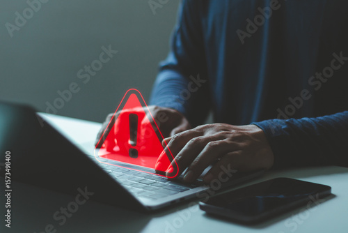 Person using laptop with red warning alert triangle icon indicating cybersecurity threat, system error, data breach. online security, digital risk, hacker attack, cyber crime protection technology.