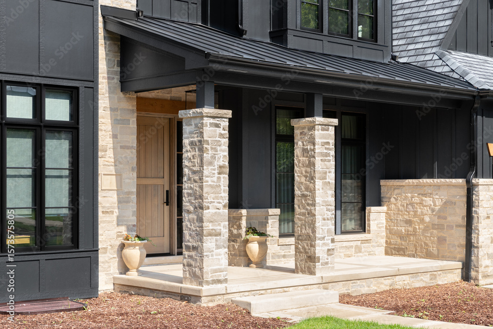 Obraz premium A front door detail on a home with black board and batten siding with natural stone accents and a beautiful oak front door.