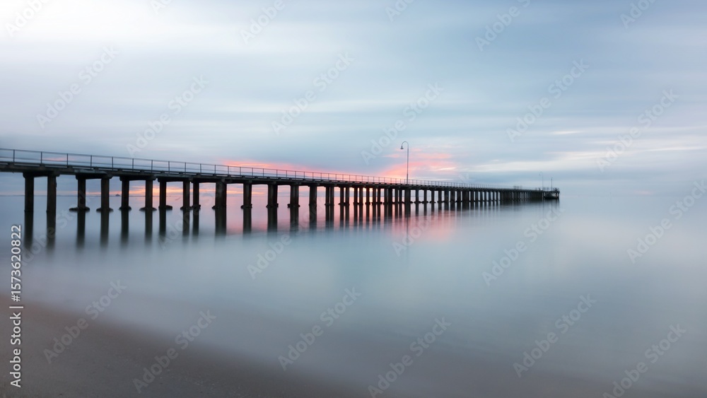 Fototapeta premium Sunset Reflection, Pier, Coastal Beach, Photography, Tranquil Water, Long Exposure, Serene Atmosphere