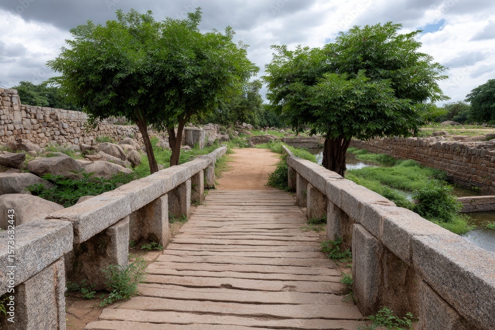 Obraz premium Stone bridge spans a waterway framed by trees and weathered stone walls under a cloudy sky