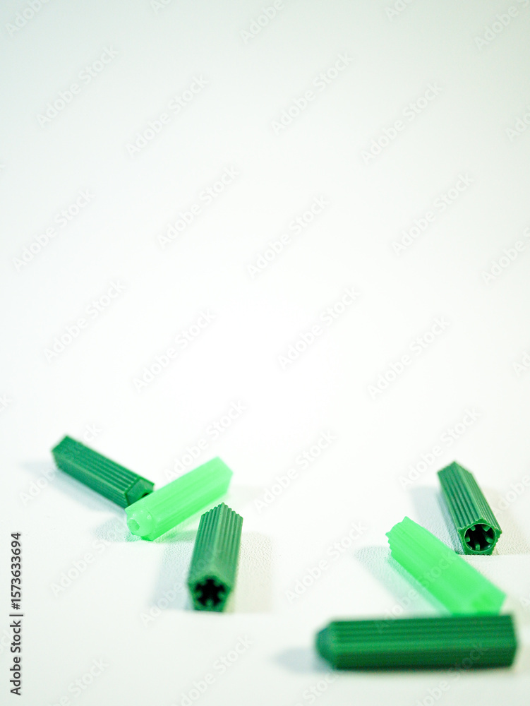 Group of green plastic wall plugs lying scattered on a plain white surface, ready for construction or DIY projects Group of green plastic wall plugs lying scattered on a plain white surface, ready for construction or DIY projects