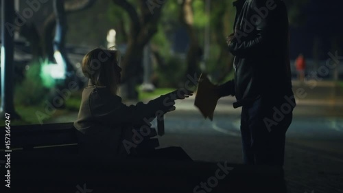 Shady handoff in a dark park — a woman on a bench discreetly passes an envelope to a standing man. Nighttime secret meeting with suspenseful, criminal or espionage undertones. secret agent word. night