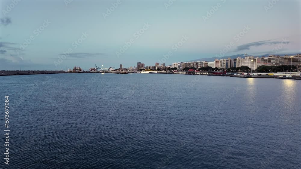 Evening shot of Santa Cruz de Tenerife’s waterfront with city skyline, port, and distant Auditorio de Tenerife. Calm sea and soft city lights create a cinematic coastal view. Evening shot of Santa Cruz de Tenerife’s waterfront with city skyline, port, and distant Auditorio de Tenerife. Calm sea and soft city lights create a cinematic coastal view.