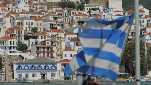 Skopelos, Greece - August 25, 2018: Greece flag waving in front of Skopelos town buildings