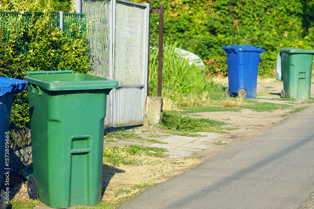 Individual garbage bins, blue and green, standing on the side of the road. Municipal waste collection and cleanliness service in environmentally friendly neighborhood. Concept of public sanitation Individual garbage bins, blue and green, standing on the side of the road. Municipal waste collection and cleanliness service in environmentally friendly neighborhood. Concept of public sanitation