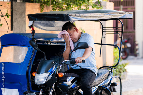Foto A tired Southeast Asian tricycle driver in casual wear wipes sweat from his face, suffering from heat exhaustion under intense summer heat