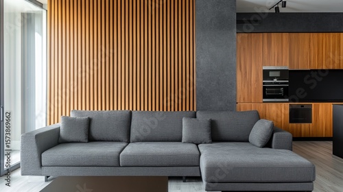 Modern living room with grey sectional sofa, wooden slat wall, and dark kitchen cabinetry