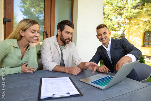 Fotografie Real estate agent discussing deal with couple on laptop outside home