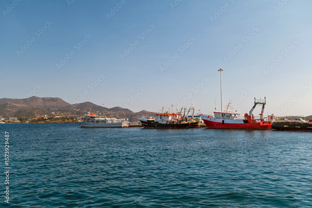 Fototapeta premium Fishing boats docked in Agios Nikolaos harbor during sunny day in Crete, Greece