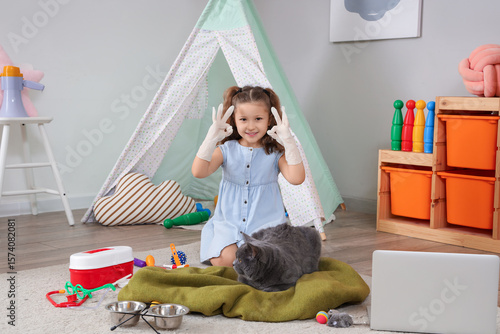 Cute little girl with British cat, laptop and first aid kit showing OK gestur...