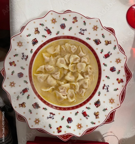 Traditional Italian tortellini in homemade capon broth served in a decorated Christmas plate, festive holiday meal, top view of typical Italian cuisine for Christmas lunch or winter family dinner