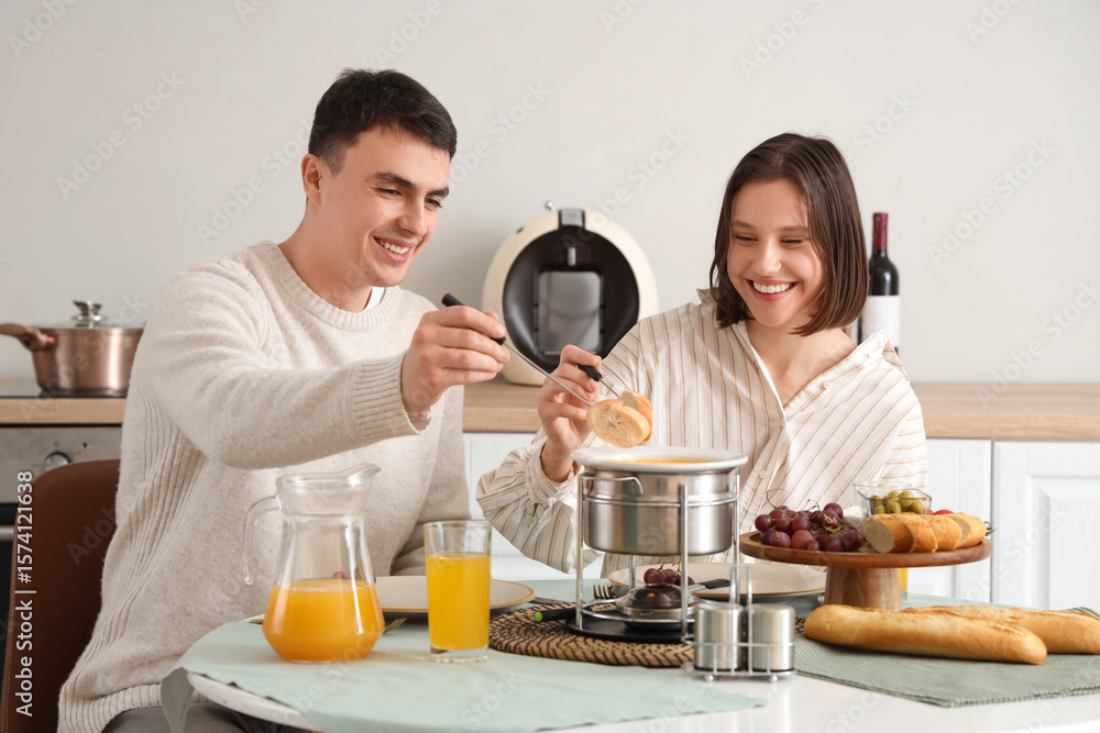 Young happy couple with glasses of juice dipping croutons into cheese fondue at home Young happy couple with glasses of juice dipping croutons into cheese fondue at home
