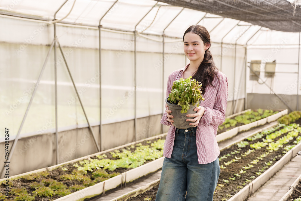 Obraz premium Multiracial teenage girl proudly holding green leafy vegetable pot in school greenhouse reflecting practical farming education organic gardening lessons and sustainable vegetable cultivation