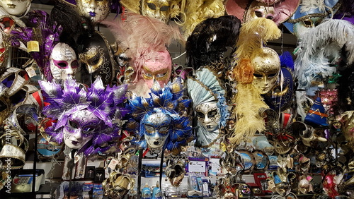 Colorful Venetian carnival masks with feathers and glitter, displayed in a vibrant souvenir shop.