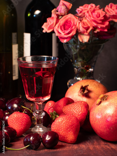 Still life with rose flowers, summer fruits, bottles of wine and a glass of wine. Pomegranate, cherry, sweet cherry, strawberry and watermelon. Alcohol. The still life is stylized as an old painting.