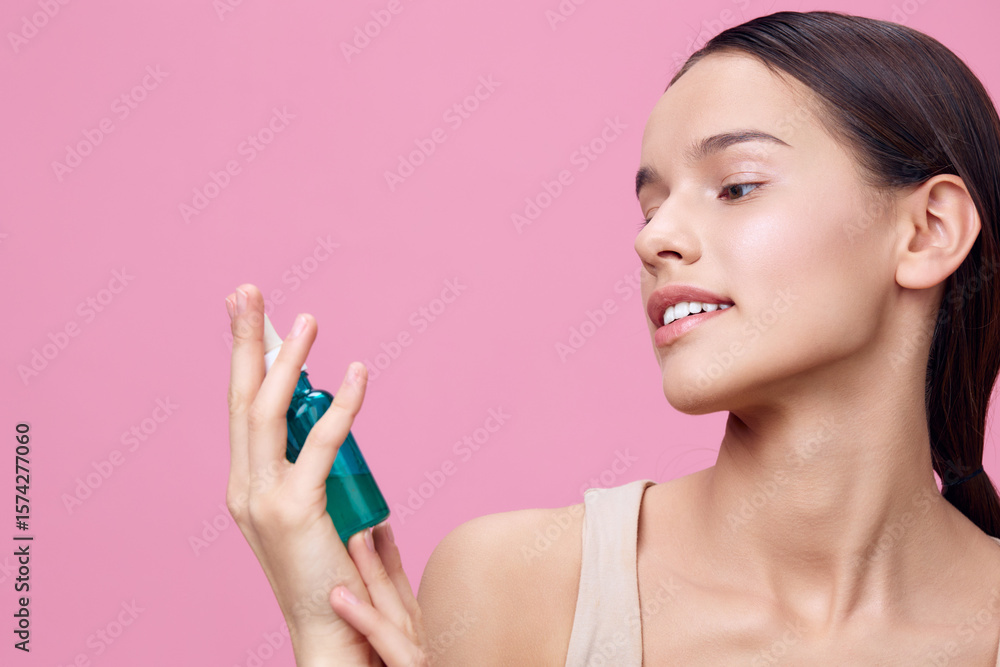 Young woman applying a green serum with a joyful expression, against a soft pink background, emphasizing skincare and beauty concepts Young woman applying a green serum with a joyful expression, against a soft pink background, emphasizing skincare and beauty concepts