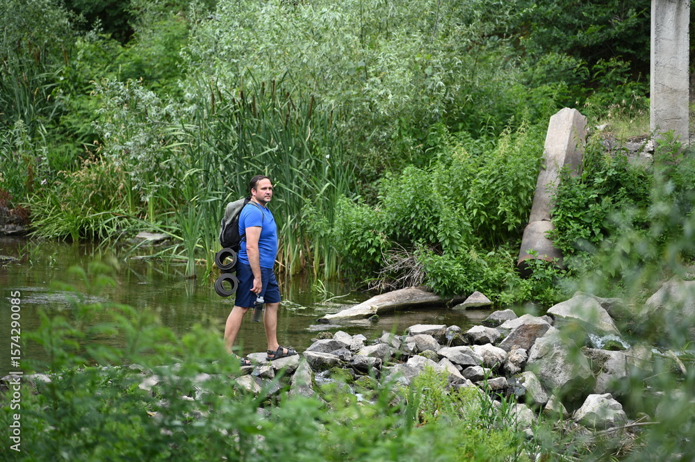 Obraz premium A man crosses a river on rocks with a backpack.