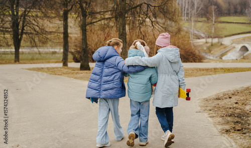 Teen girls walk together, hugging shoulders, each holding a skateboard. Jackets, jeans, sneakers show winter street style. Outdoor friendship, movement, balance, youth bonding, lifestyle and freedom