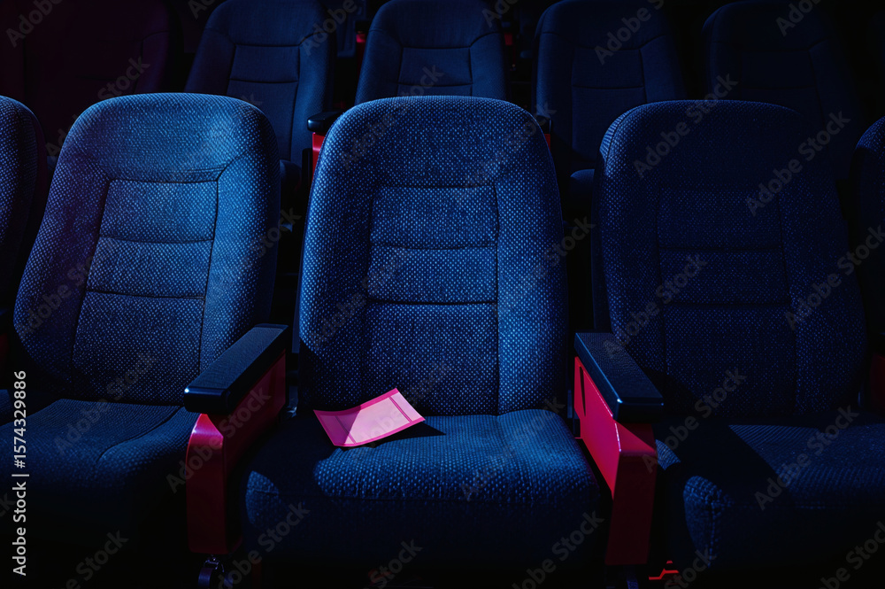 Obraz premium Torn movie ticket stub on empty theater seat in dark lighting 