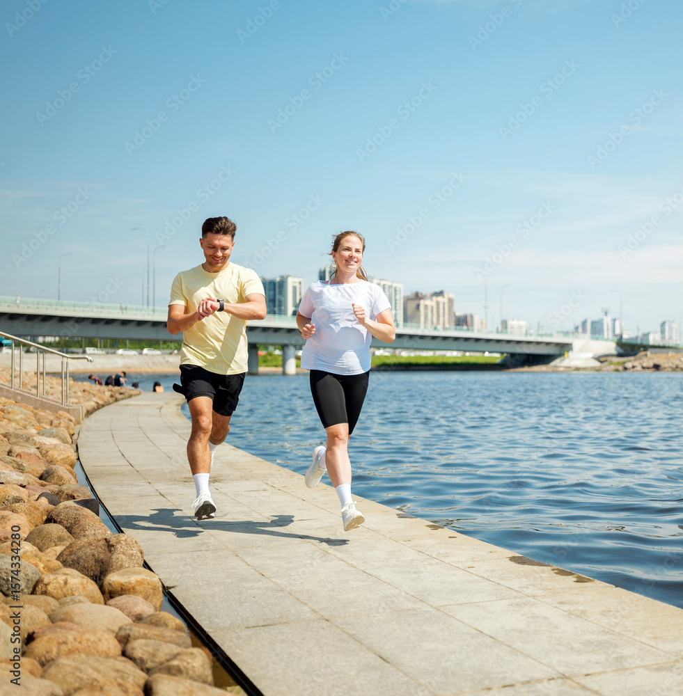 Fototapeta premium Sunny day joggers enjoying a lively run along a serene riverside pathway