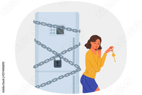 Woman starting diet locked refrigerator to reduce number of calories from food consumed. Funny girl wants to break diet and have dinner at night, due to lack of willpower and motivation