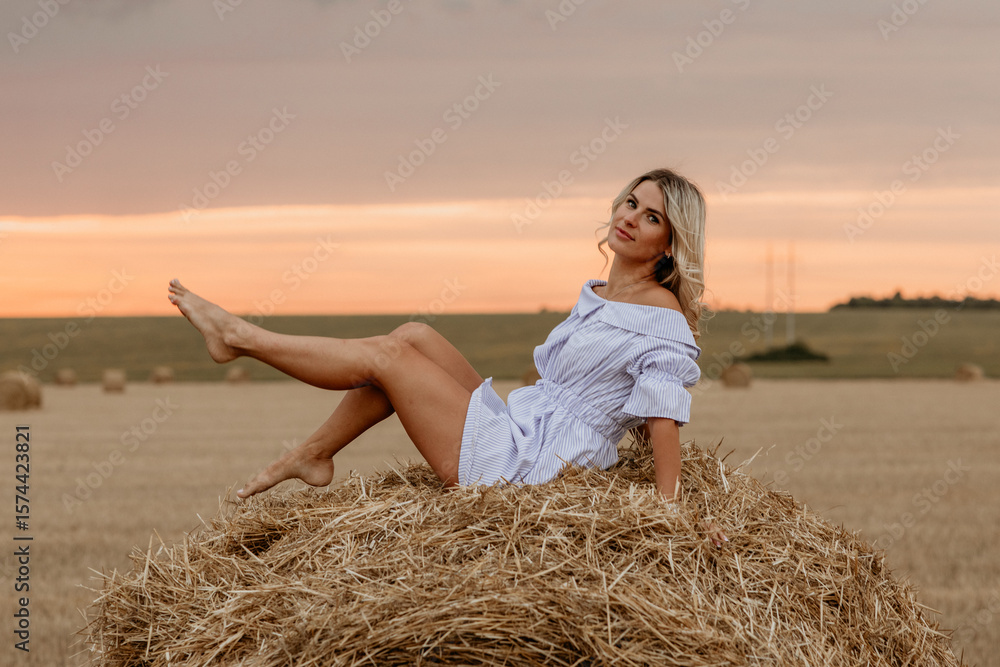 Beautiful young blonde girl in a field of haystacks at sunset in summer Beautiful young blonde girl in a field of haystacks at sunset in summer