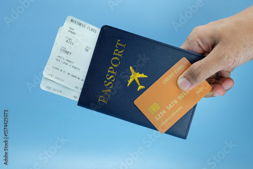 A hand holding a dark blue passport holder containing a boarding pass and a gold credit card isolated on a clean blue background.Ideal for business travel, airport preparation, identity verification