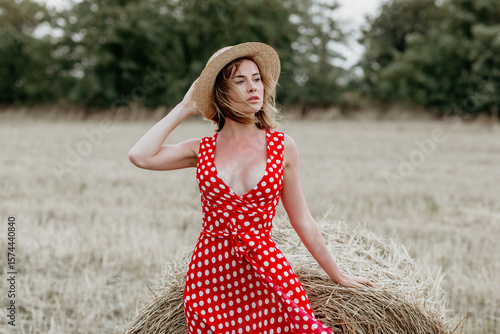 Wall Mural Beautiful young girl in a red polka dot dress and hat in a field of haystacks