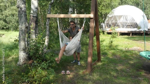Father and daughter. Girl relaxing in hammock using smartphone at forest camping.  Father rocks hammock with his daughter. 