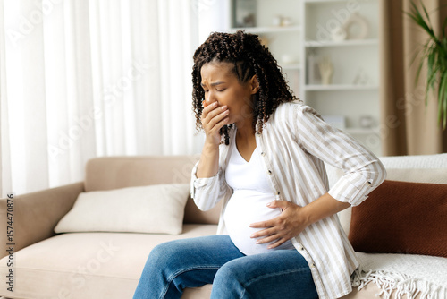 Fototapeta Black pregnant woman covering mouth in discomfort, experiencing nausea