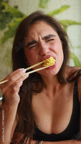 A girl eats a hot dish with chopsticks and shows an expression of displeasure after burning her mouth.