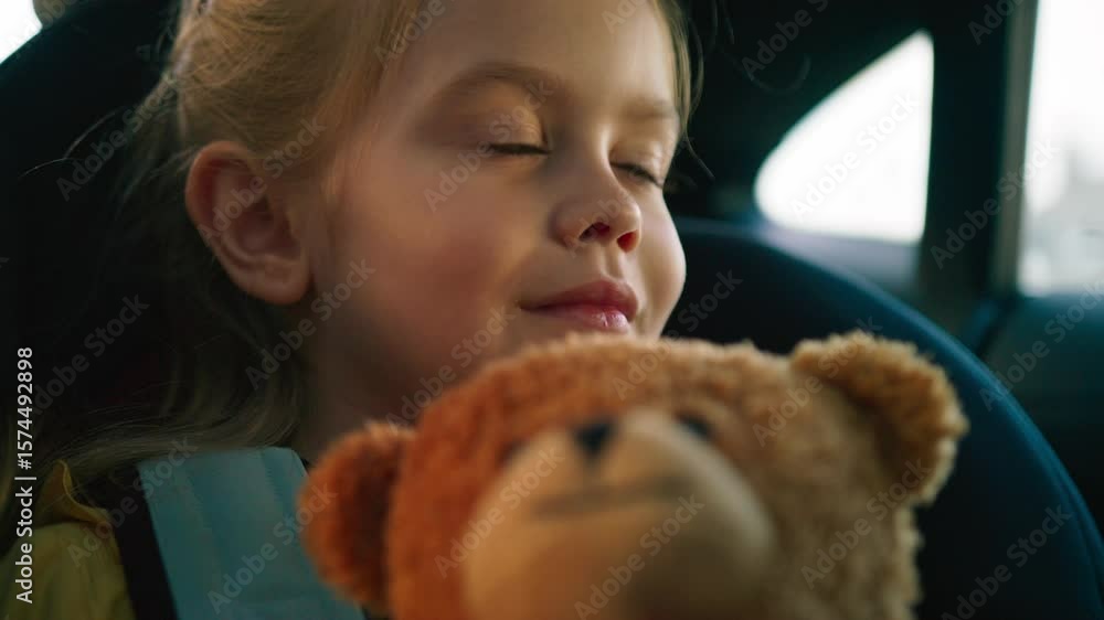 Girl with bright eyes holding soft teddy bear while riding in car seat. Gazing out window calmly. Cuddling plush toy close to chest. Enjoying quiet car ride through residential area. Girl with bright eyes holding soft teddy bear while riding in car seat. Gazing out window calmly. Cuddling plush toy close to chest. Enjoying quiet car ride through residential area.