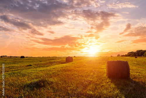 Scenic sunset over hay bales in a field. Golden light bathes the landscape, creating a tranquil scene. For agriculture, travel and inspiring greeting card designs.