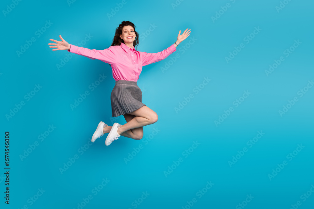 Obraz premium Playful student in stylish attire jumps joyfully over a vibrant blue background showcasing her lively personality