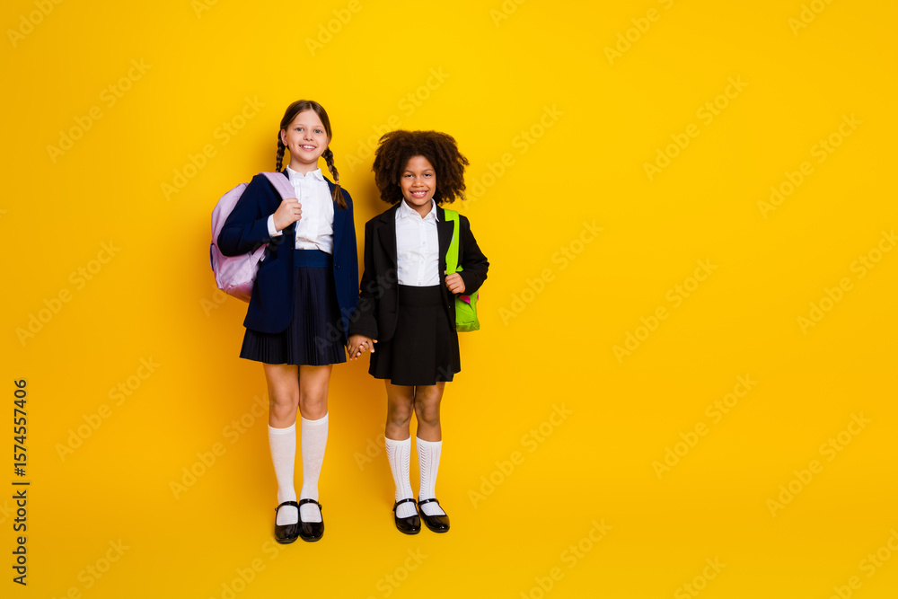 Obraz premium Diverse preteen schoolgirls standing together holding hands in school uniforms on bright yellow background