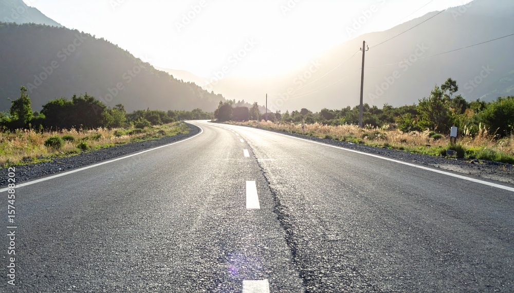 Naklejka premium Scenic asphalt road curves through a lush landscape toward distant mountains and a bright, inviting horizon.