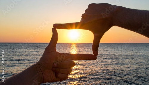 Hands create a frame around a gorgeous sunset over a tranquil sea, capturing the beauty and serenity of the ocean horizon.