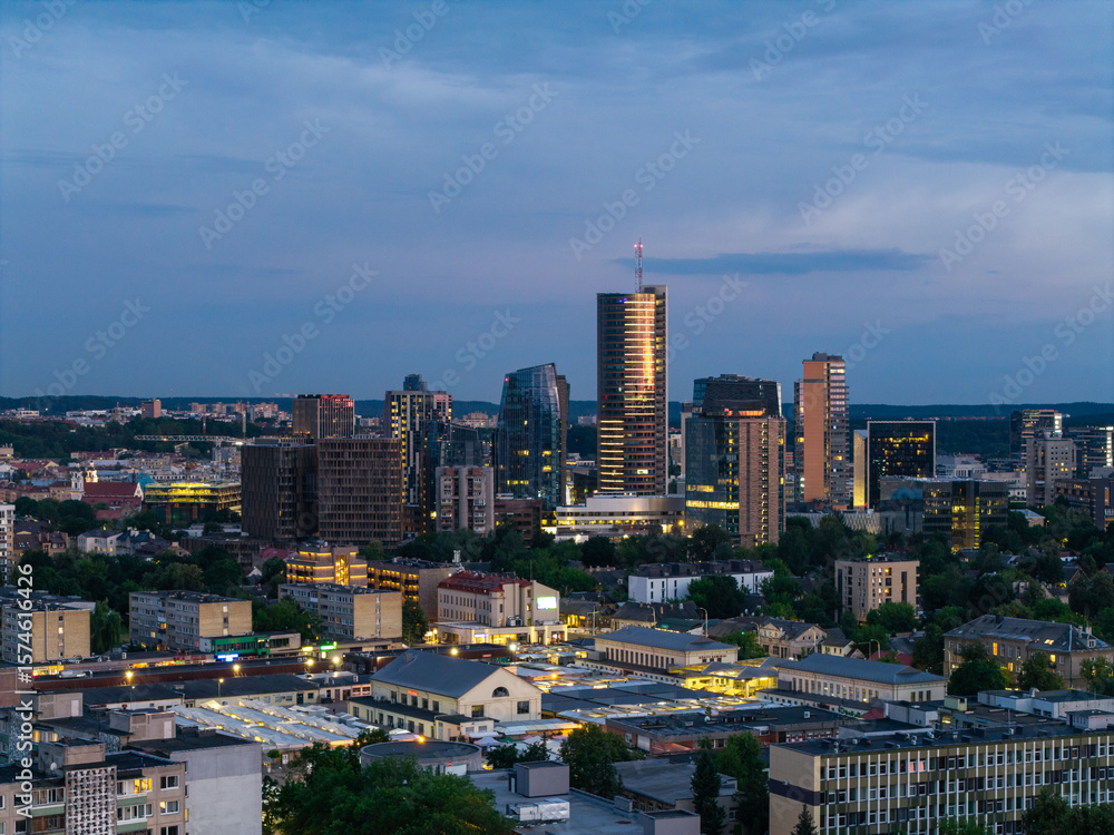 Fototapeta premium Twilight view of the Vilnius business district with modern skyscrapers and buildings lit up as night falls. Captured during the blue hour, showcasing the vibrant energy of Lithuania’s capital.