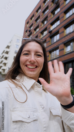 Close-up portrait of attractive young Caucasian girl smiling and looking at camera, taking selfie video. Cute woman broadcasting video with smartphone, waving at webcam