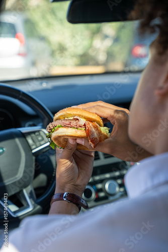 Photography Zoom sur un homme assis dans sa voiture tenant un burger dans sa main, prêt à manger, dans une ambiance urbaine et décontractée
