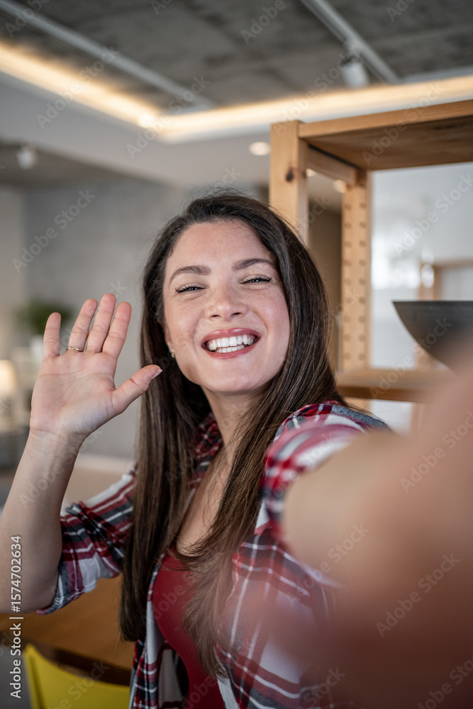 Cheerful woman waving hand while taking selfie at home Cheerful woman waving hand while taking selfie at home
