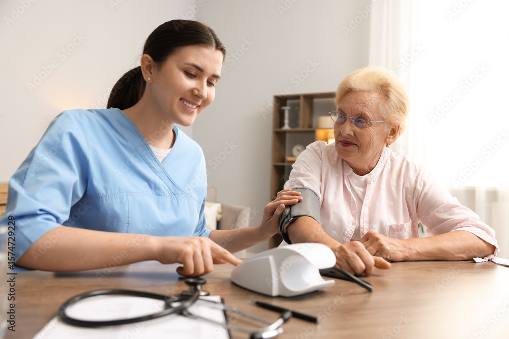 Fototapeta premium Nurse measuring patient's blood pressure at wooden table indoors. Home health care service