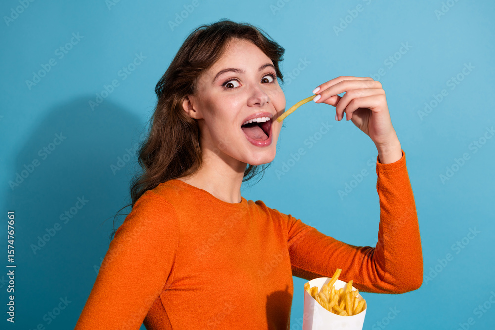 Φωτογραφία Young woman in orange top enjoying French fries against a blue background, empha