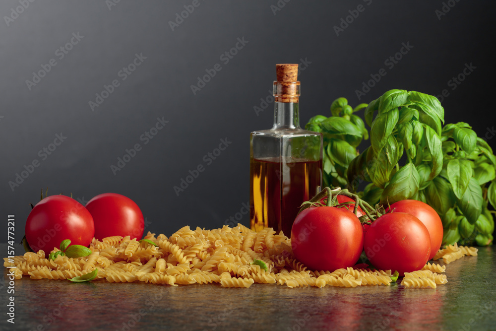Fototapeta premium Fusilli pasta with olive oil, tomatoes and basil on a black background.
