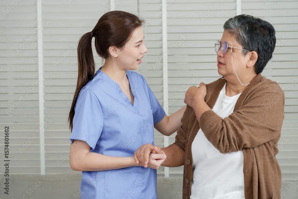 Asian female physical therapist gently supports senior asian woman during arm rehabilitation exercise as she stretches shoulder using one arm across chest in recovery session Asian female physical therapist gently supports senior asian woman during arm rehabilitation exercise as she stretches shoulder using one arm across chest in recovery session